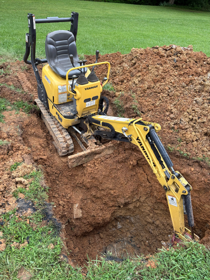 Compact excavator carefully uncovering a septic tank